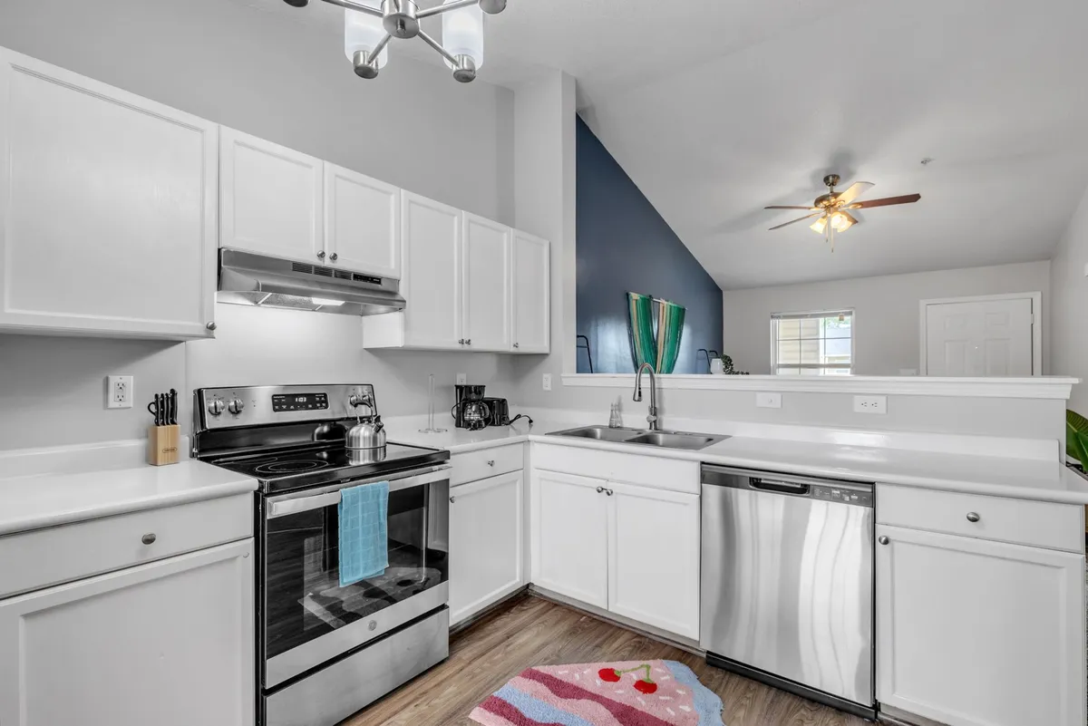 A modern kitchen setup with stainless steel appliances, a central island for prep or gathering, a lively colorful rug, and a blue accent wall. The setting is lively and designed for both cooking and sharing meals together.