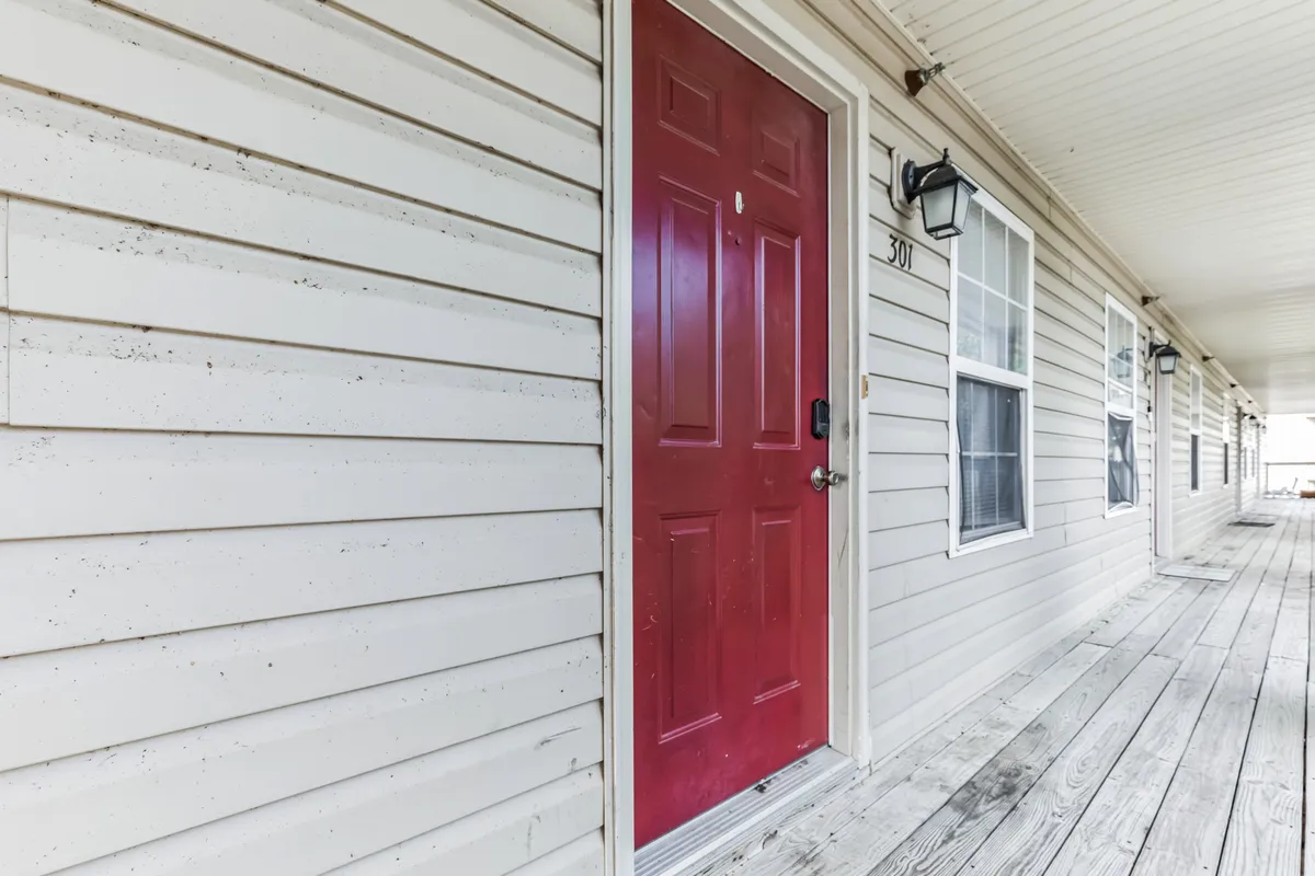 A welcoming red door and wooden porch mark the entrance, with neighbors enjoying casual conversations and quiet moments outside. The inviting facade sets the tone for first impressions and community interaction.