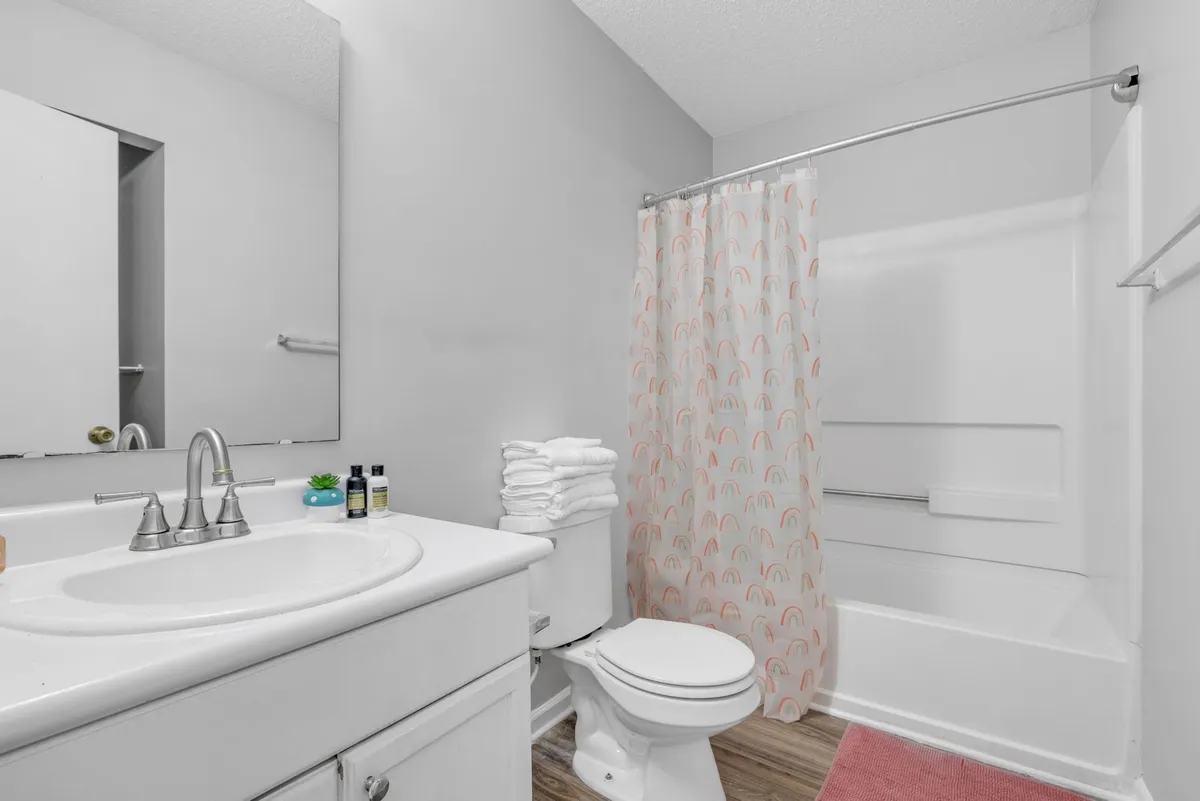 A bright, fresh bathroom featuring a sink, toilet, shower curtain, and neatly folded towels. The space is well-lit and evokes a spa-like feel, suggesting a clean and inviting environment for daily routines.